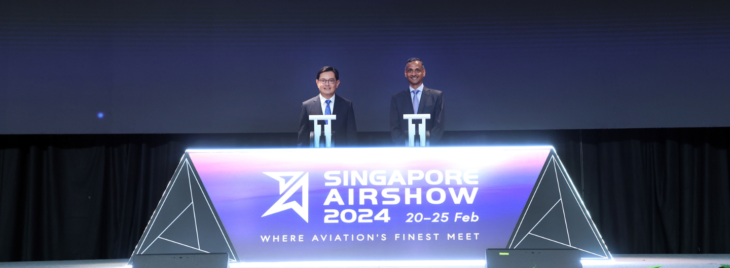 Two men at "Singapore Airshow 2024" podium on a stage with dark curtain backdrop.